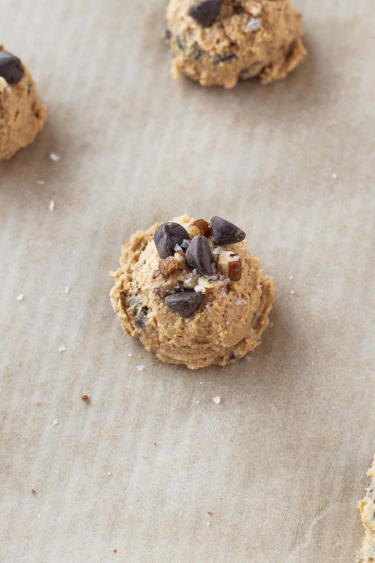 closeup on an unbaked oat flour chocolate chip cookie that has been topped with extra chocolate chips and pecans.