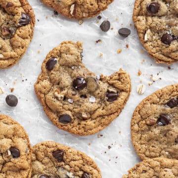 overhead closeup shot of oat flour chocolate chip cookies on a crumpled parchment paper with a bowl of rolled oats.