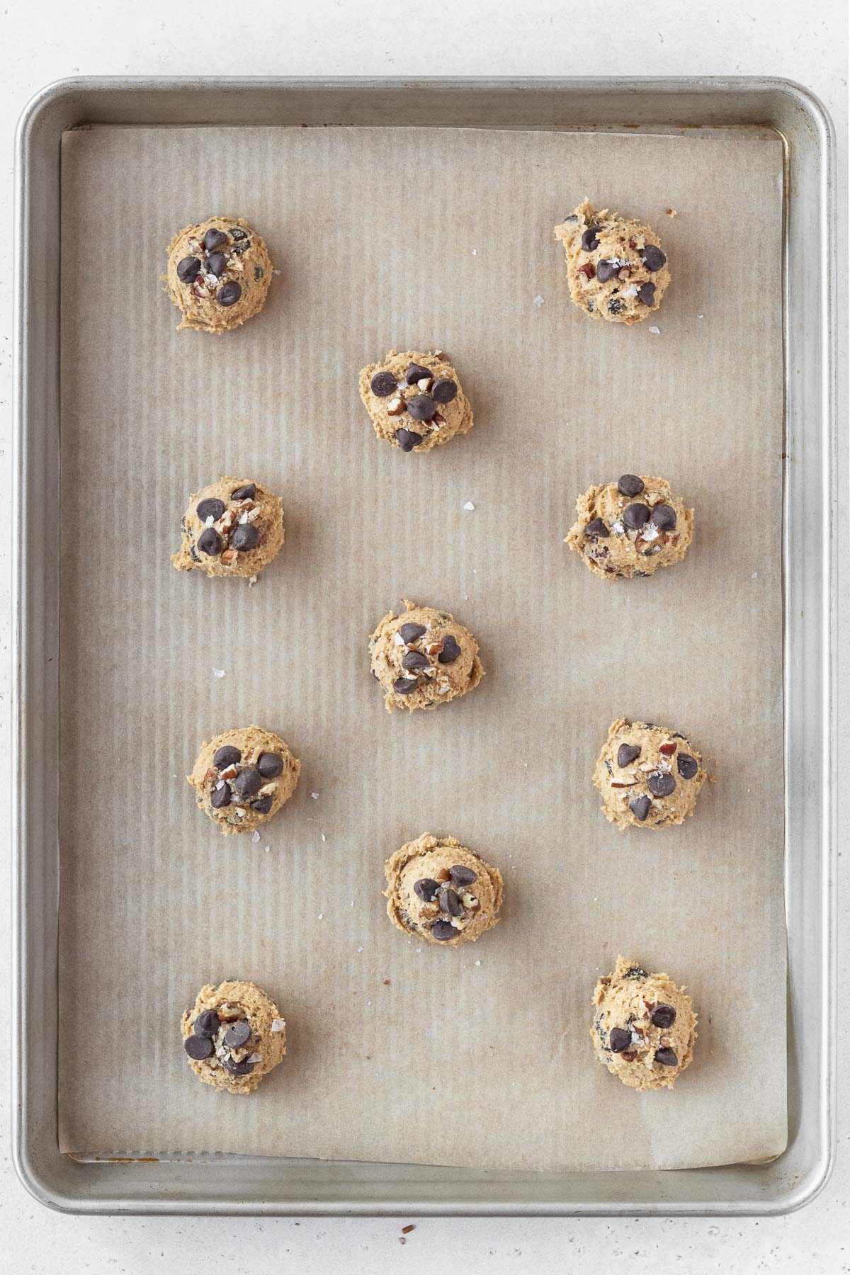 balls of oat flour chocolate chip cookie dough on a parchment lined baking sheet.