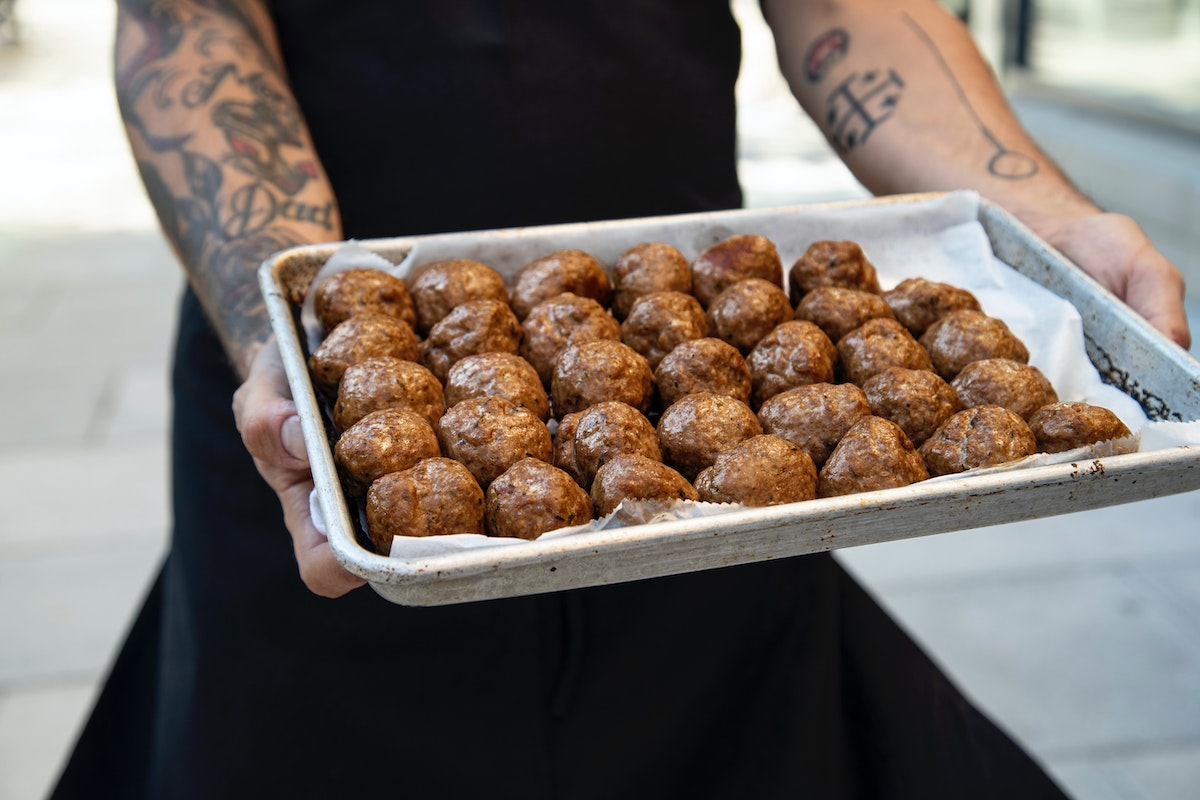 tattooed arms holding a tray of meatballs made without eggs. 