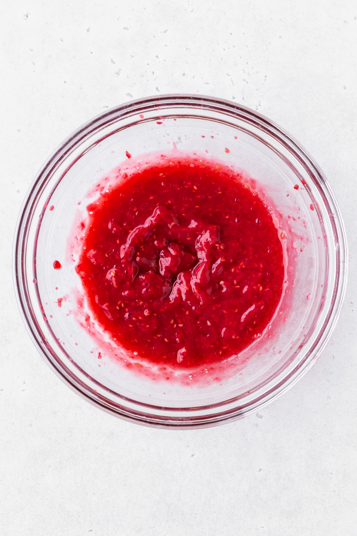 overhead shot of pureed raspberries in a clear bowl.