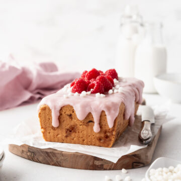 square hero shot of eggless raspberry white chocolate loaf pound cake on a cutting board with a silver knife.