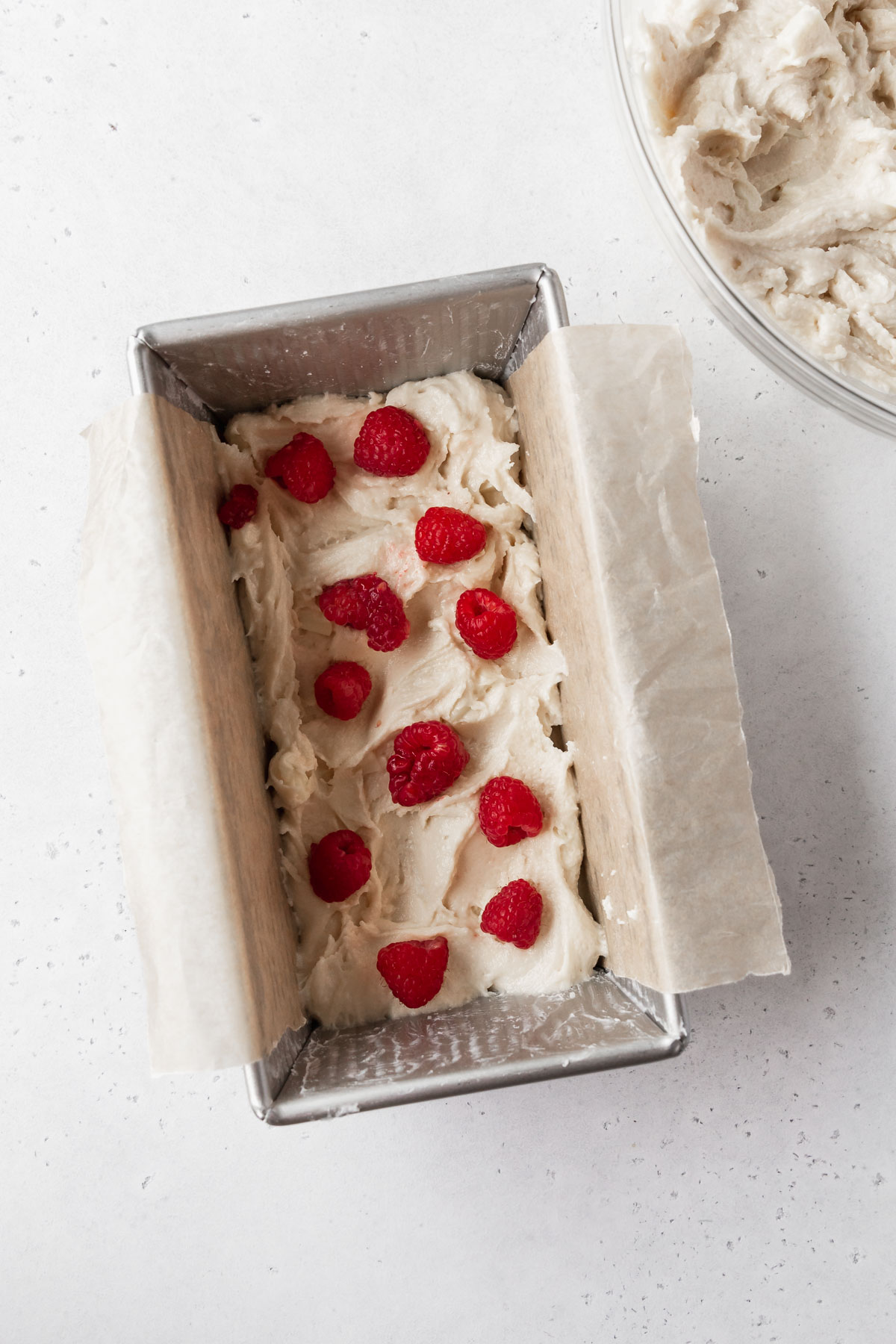 step 5 — first layer of white chocolate egg free pound cake batter in a loaf tin topped with some scattered fresh raspberries.d