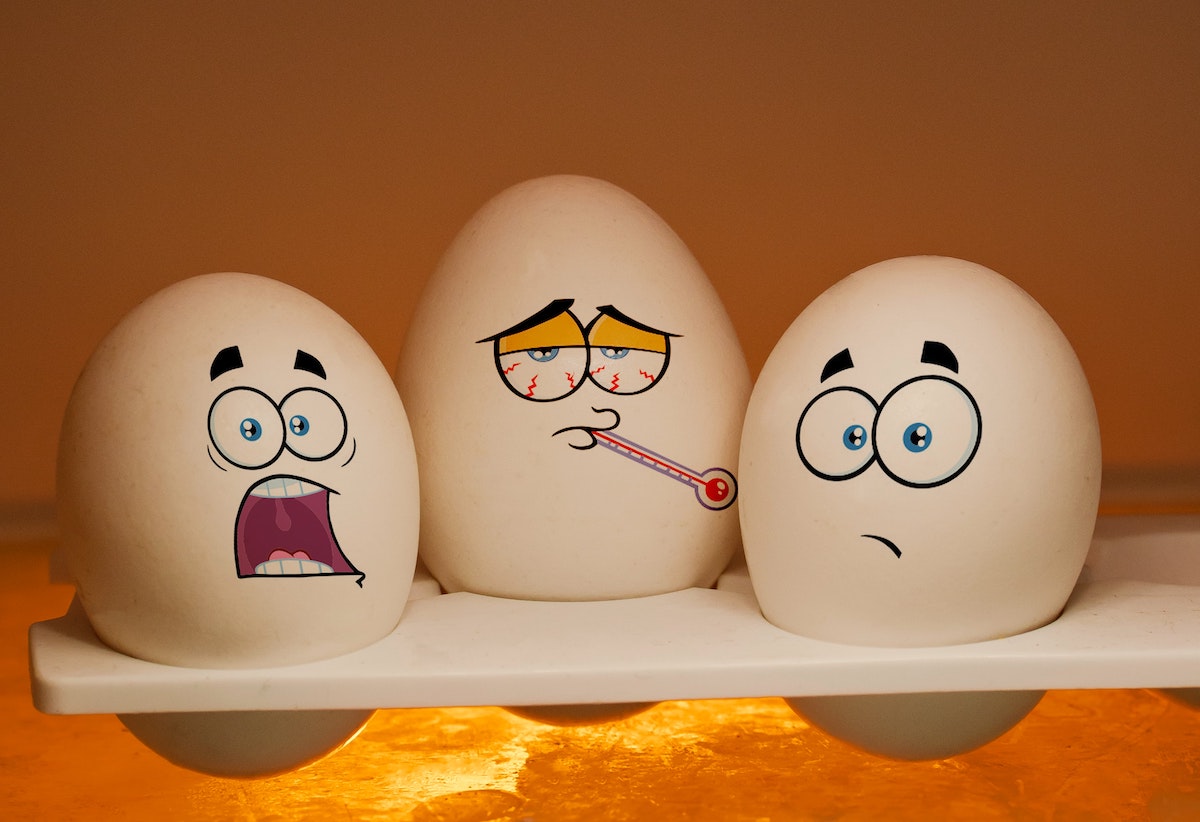 eggs in a holder with cartoon faces drawn on to look surprised, scared, and sick.