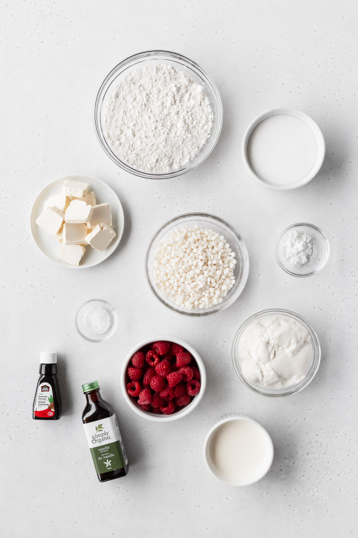 ingredients for making eggless raspberry white chocolate pound cake in a loaf tin measured out into bowls on a white table.