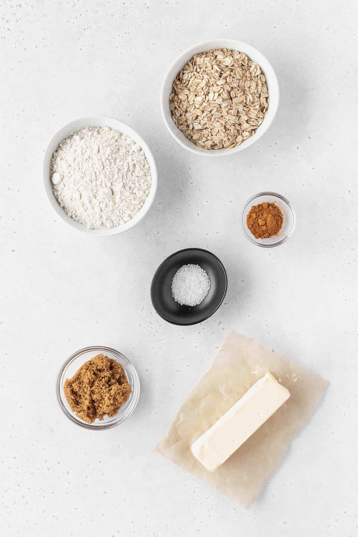 ingredients for making the oatmeal cookie crumble measured out into bowls on a white table.