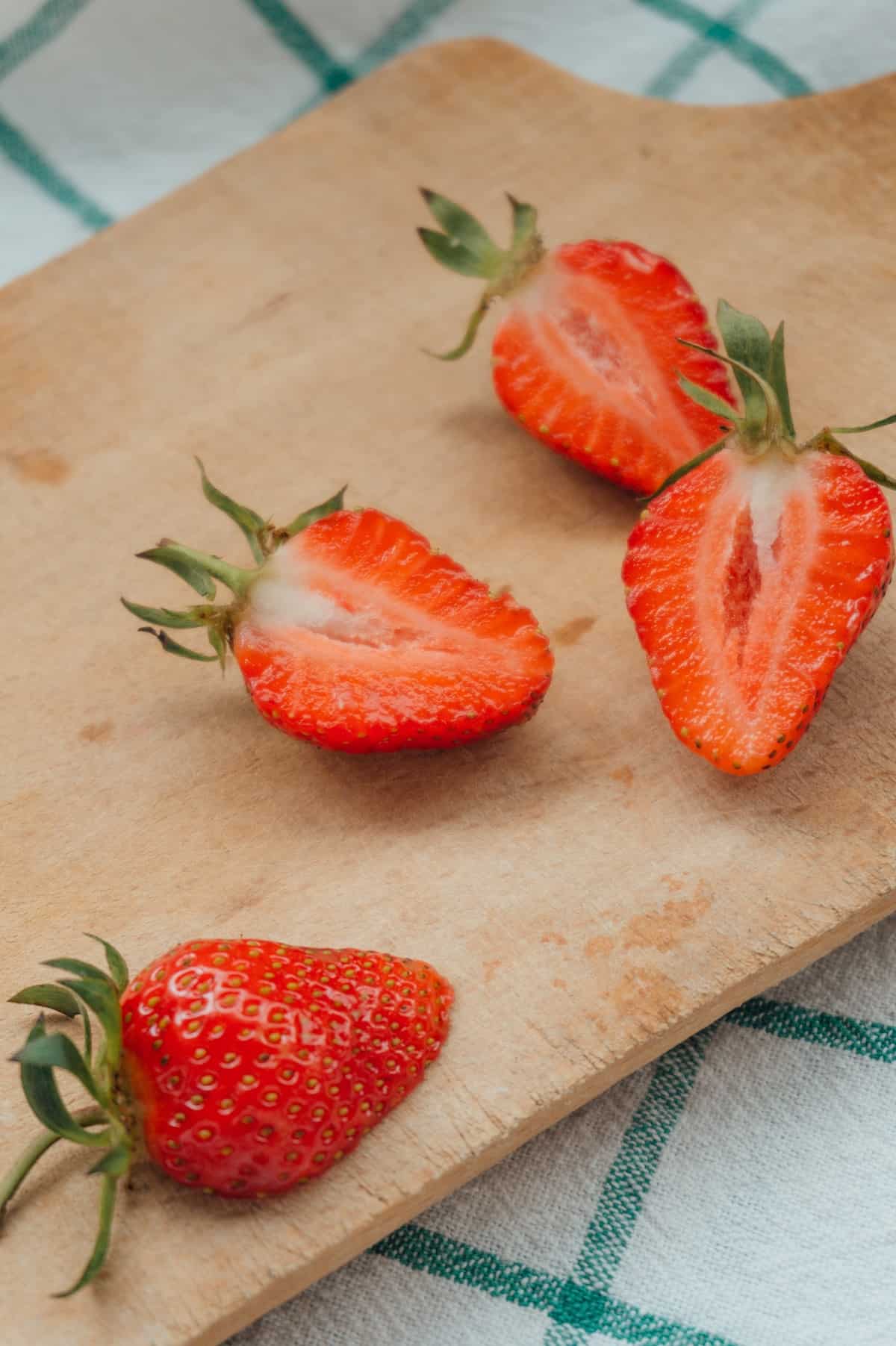 halved strawberries on a wooden cutting board. photo credit hanna balan.