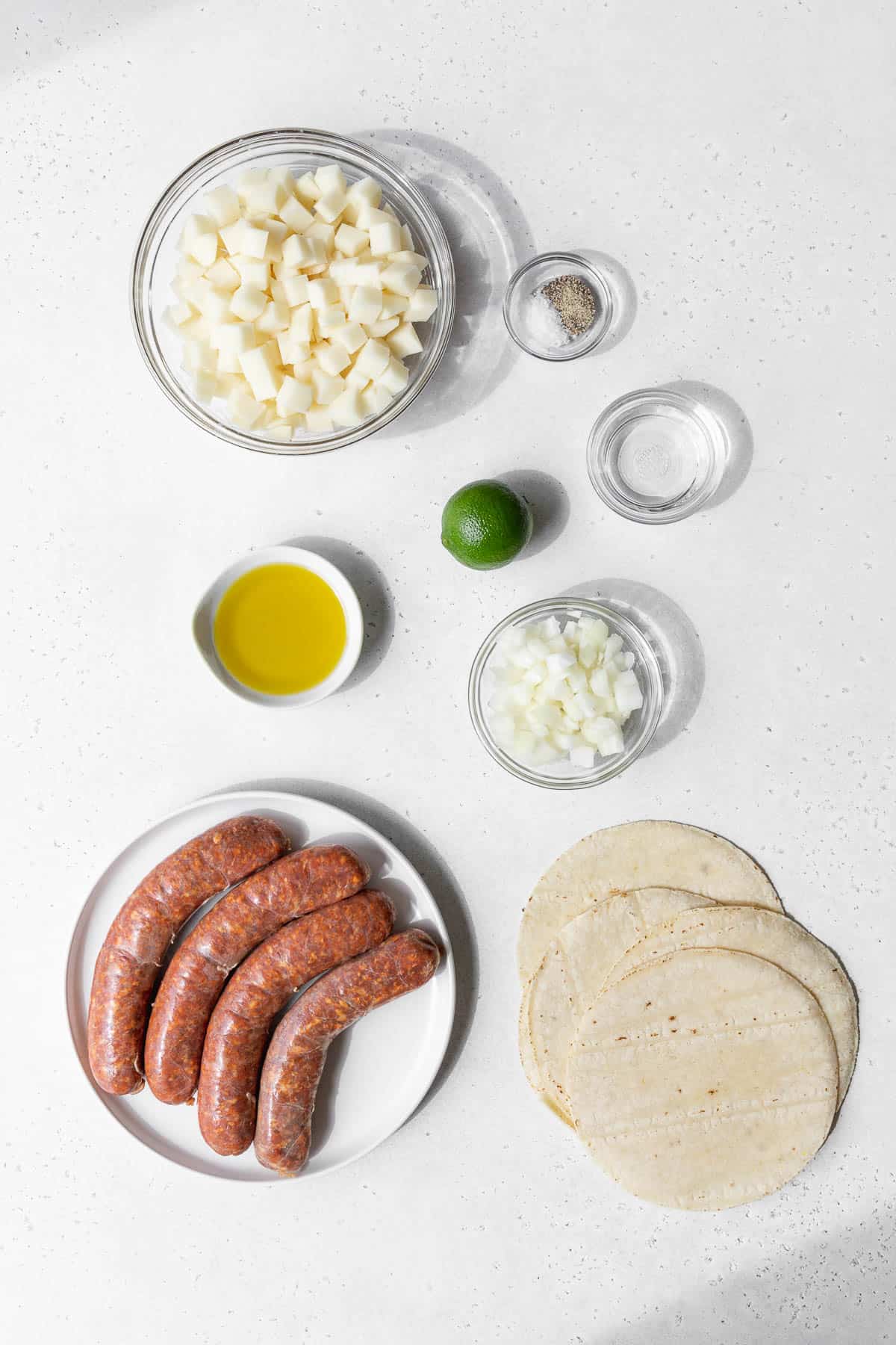 overhead shot of the ingredients needed to make spicy chorizo and potato tacos on a white table.