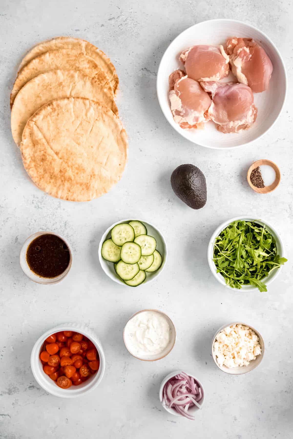 ingredients needed to make easy Greek-inspired grilled chicken pita wraps measured out into bowls on a white table.