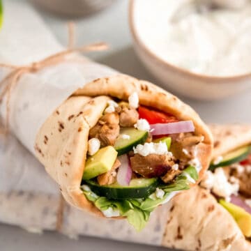 closeup square hero of easy grille chicken pita wraps that are wrapped in parchment and tied with twine.