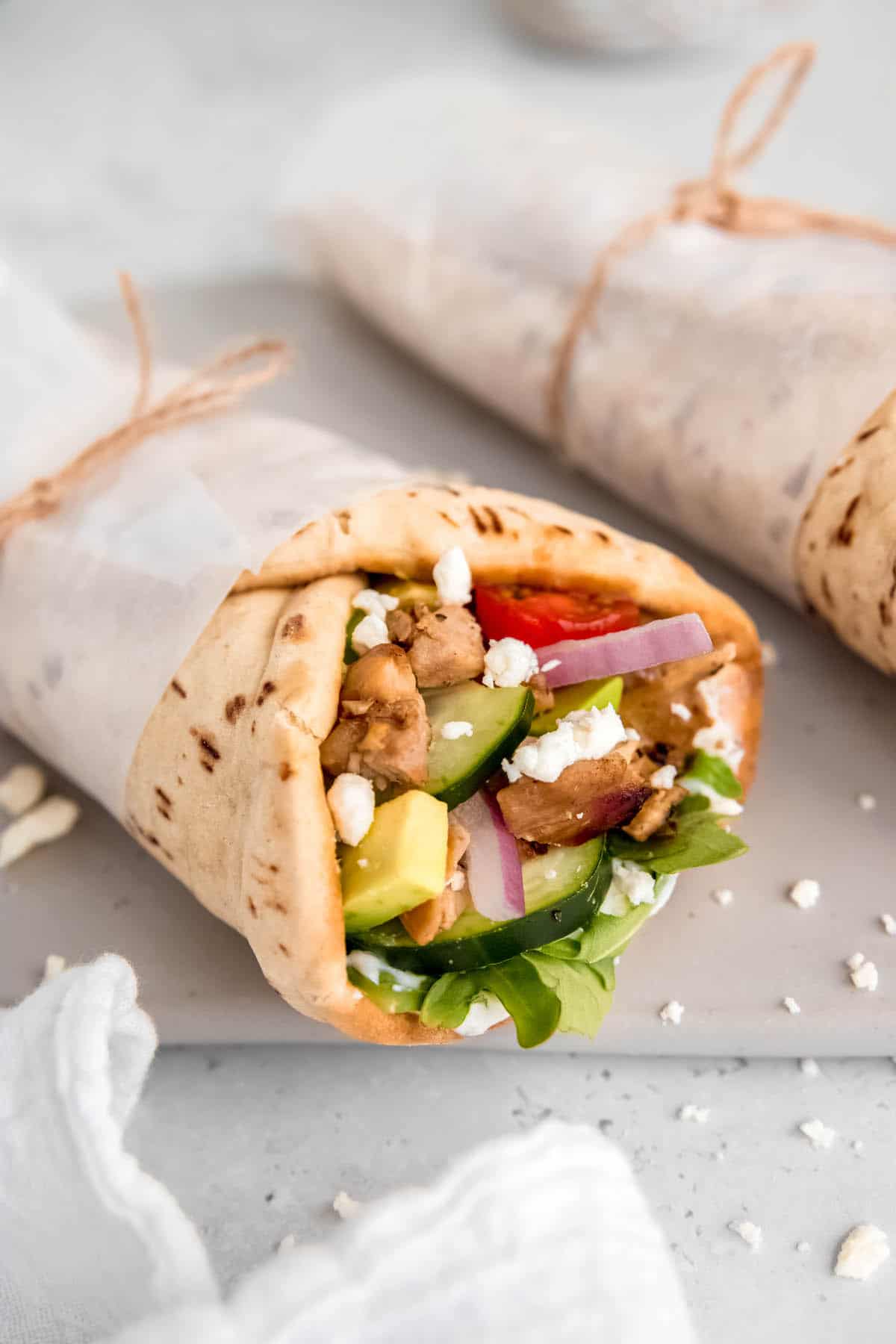 vertical closeup hero of a chicken pita wrap in parchment secured with twine.