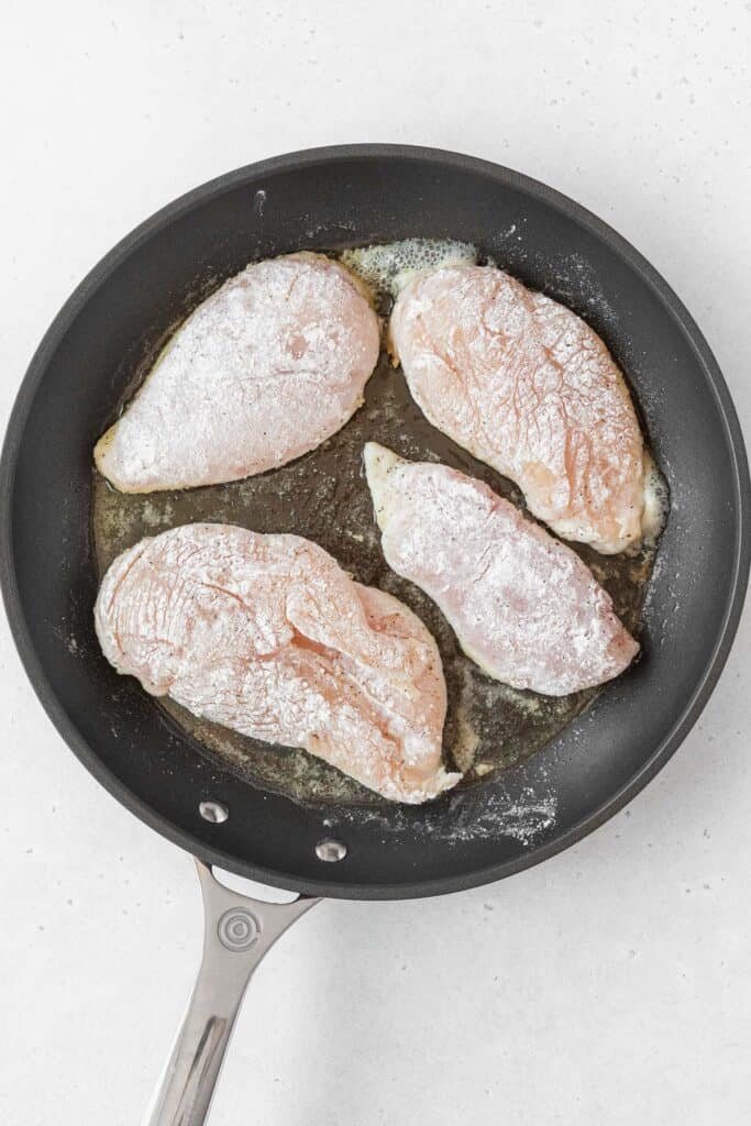 searing dredged and brined chicken breasts in a pan.
