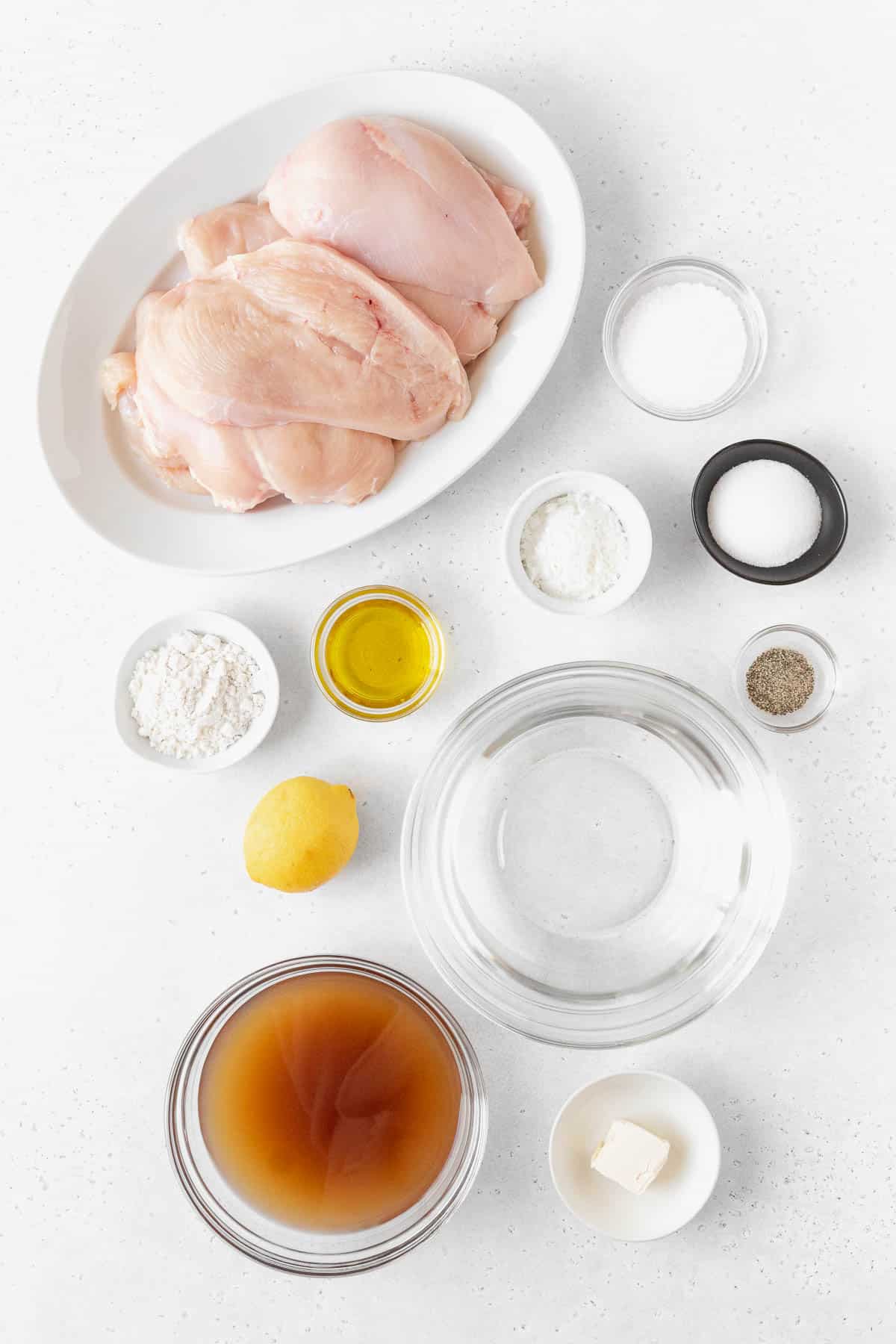 overhead shot of ingredients needed to make Italian lemon butter chicken (chicken limone) measured out into bowls on a white table.