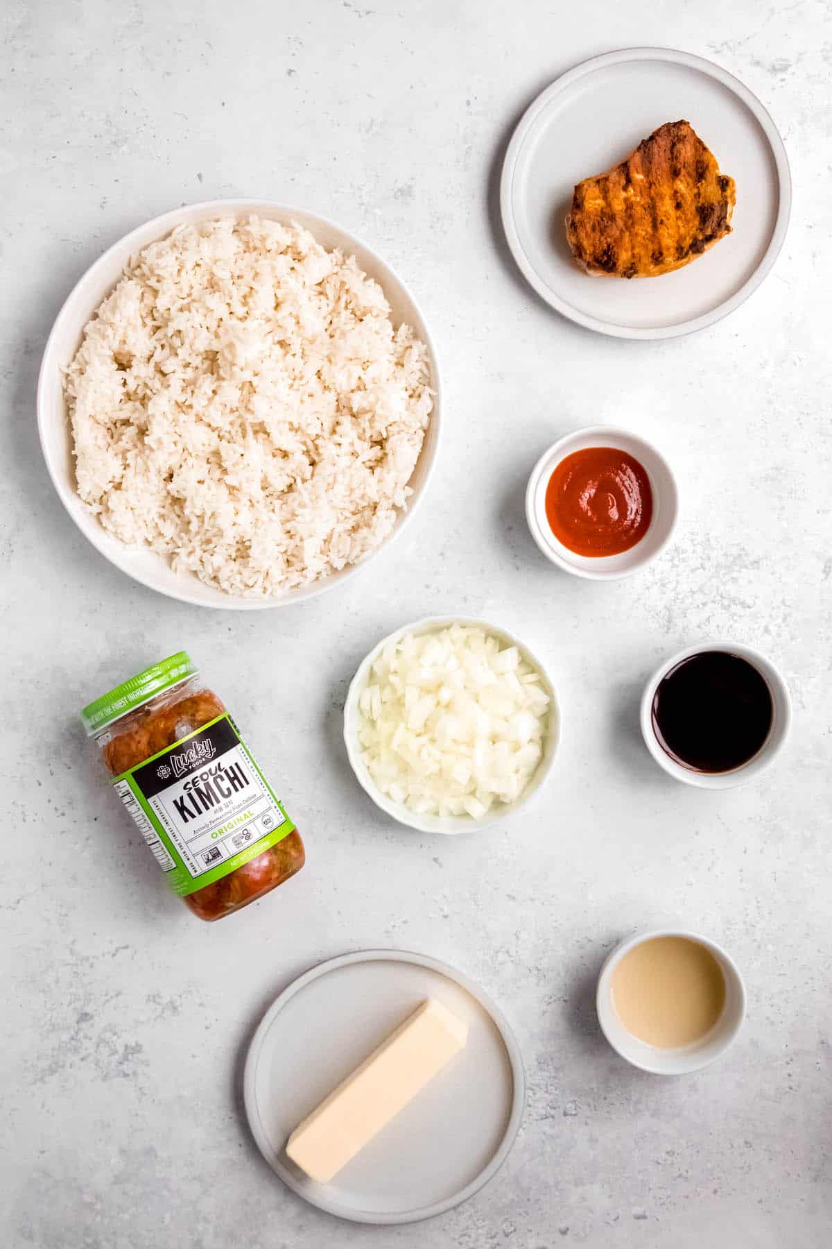 Overhead shot of ingredients needed to make Korean-inspired bbq pork fried rice measured out into bowls on a white table.