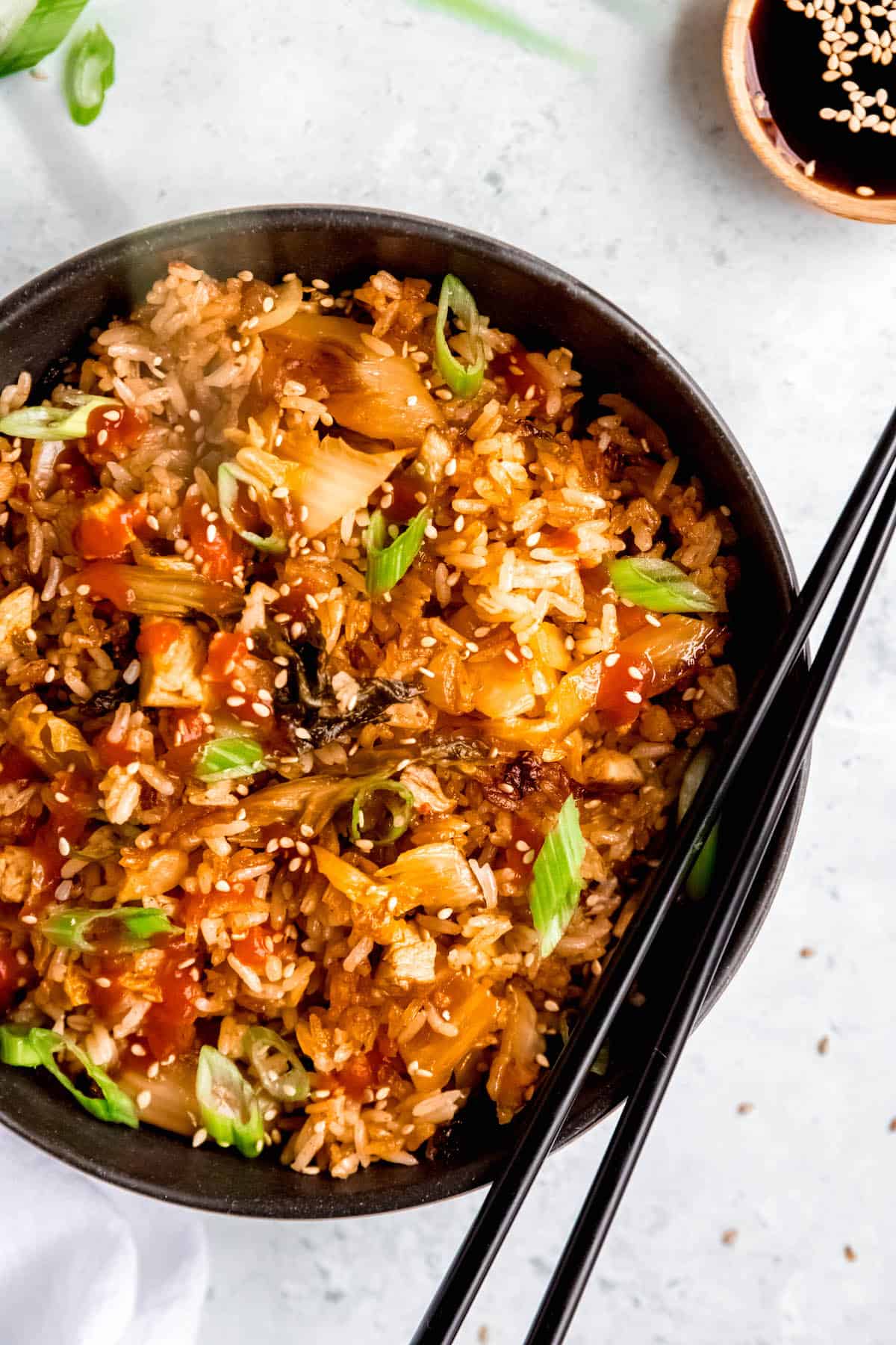 hero shot of a bowl of kimchi pork fried rice in a black bowl with a pair of black chopsticks on a white table.