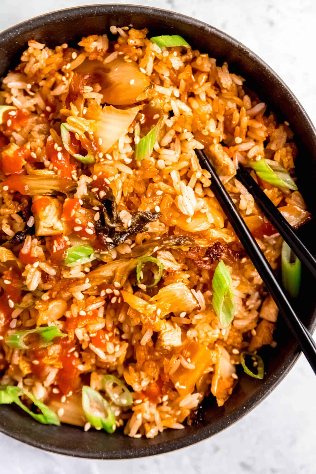 closeup shot of a pair of black chopsticks sticking out of a bowl of spicy pork fried rice made with leftover BBQ pork chops.