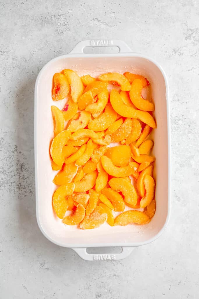 peaches spread out in the prepared cake pan.