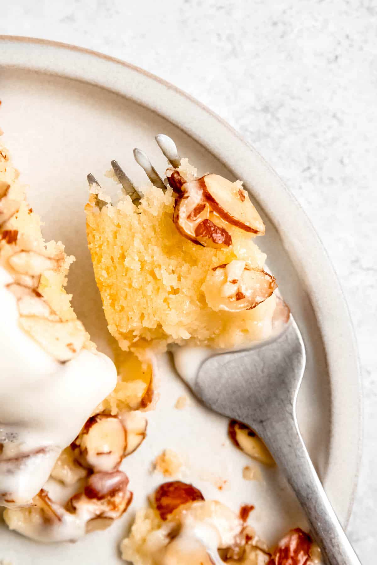 overhead shot of a bite of Italian lemon cake on a fork with some of the toffeed almond topping and whipped lemon ricotta.