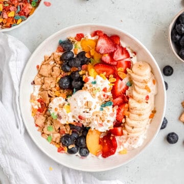 hero shot of breakfast banana split bowl with a bowl of fruity pebbles and a bowl of blueberries on the table.