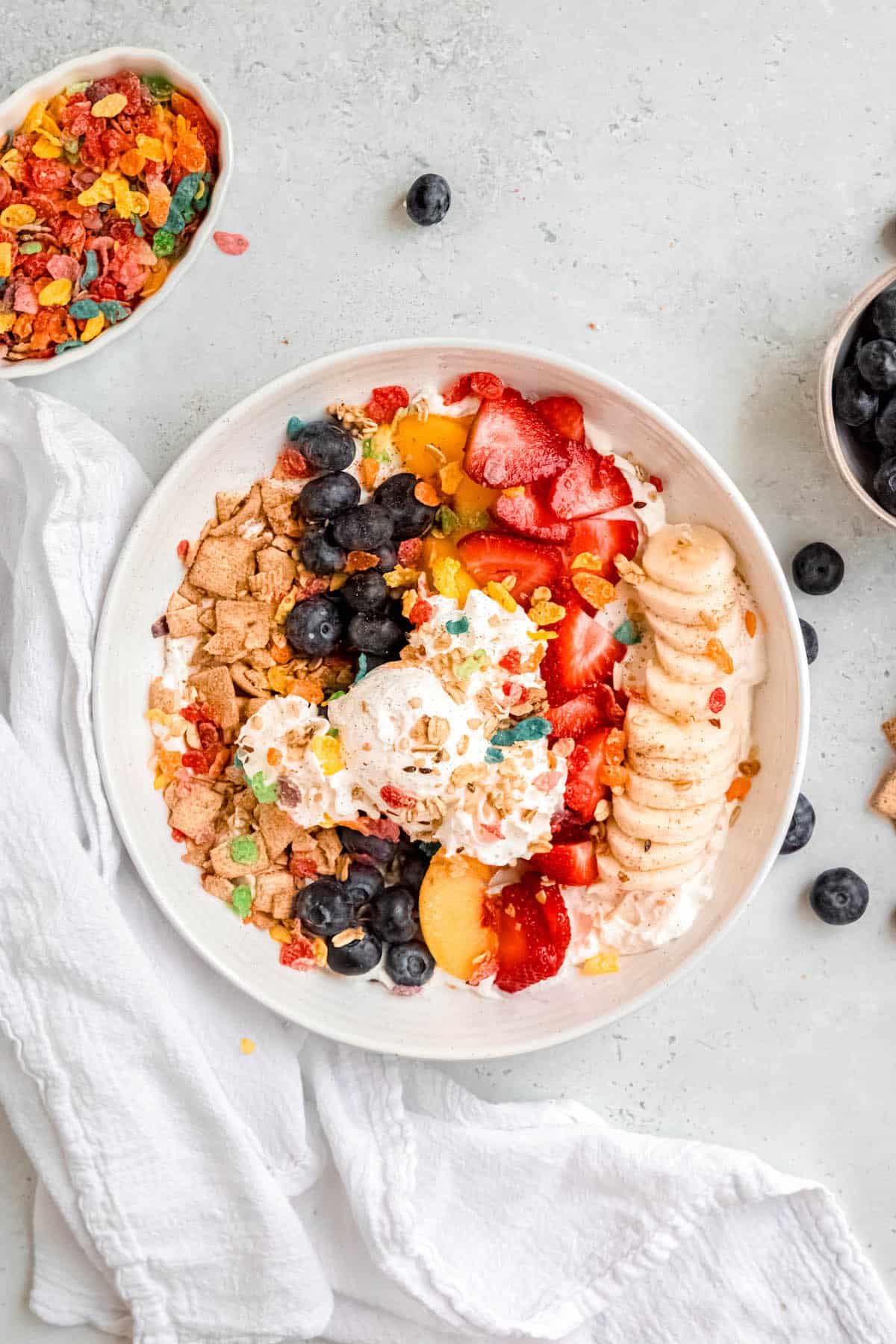hero shot of breakfast banana split bowl with a bowl of fruity pebbles and a bowl of blueberries on the table.