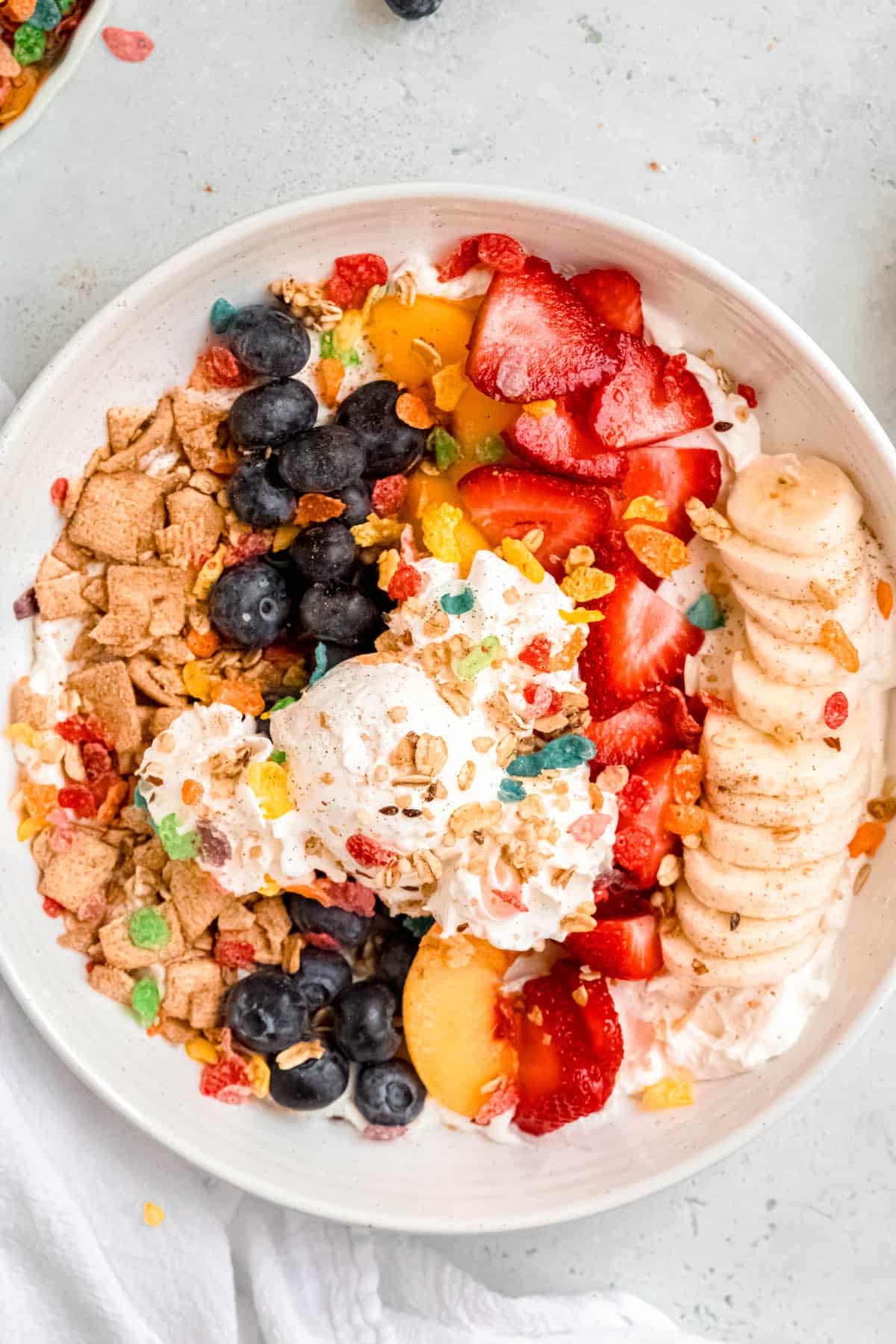 closeup overhead shot of an assembled banana split parfait with cereal, fruit, greek yogurt, and cool whip ice cream.