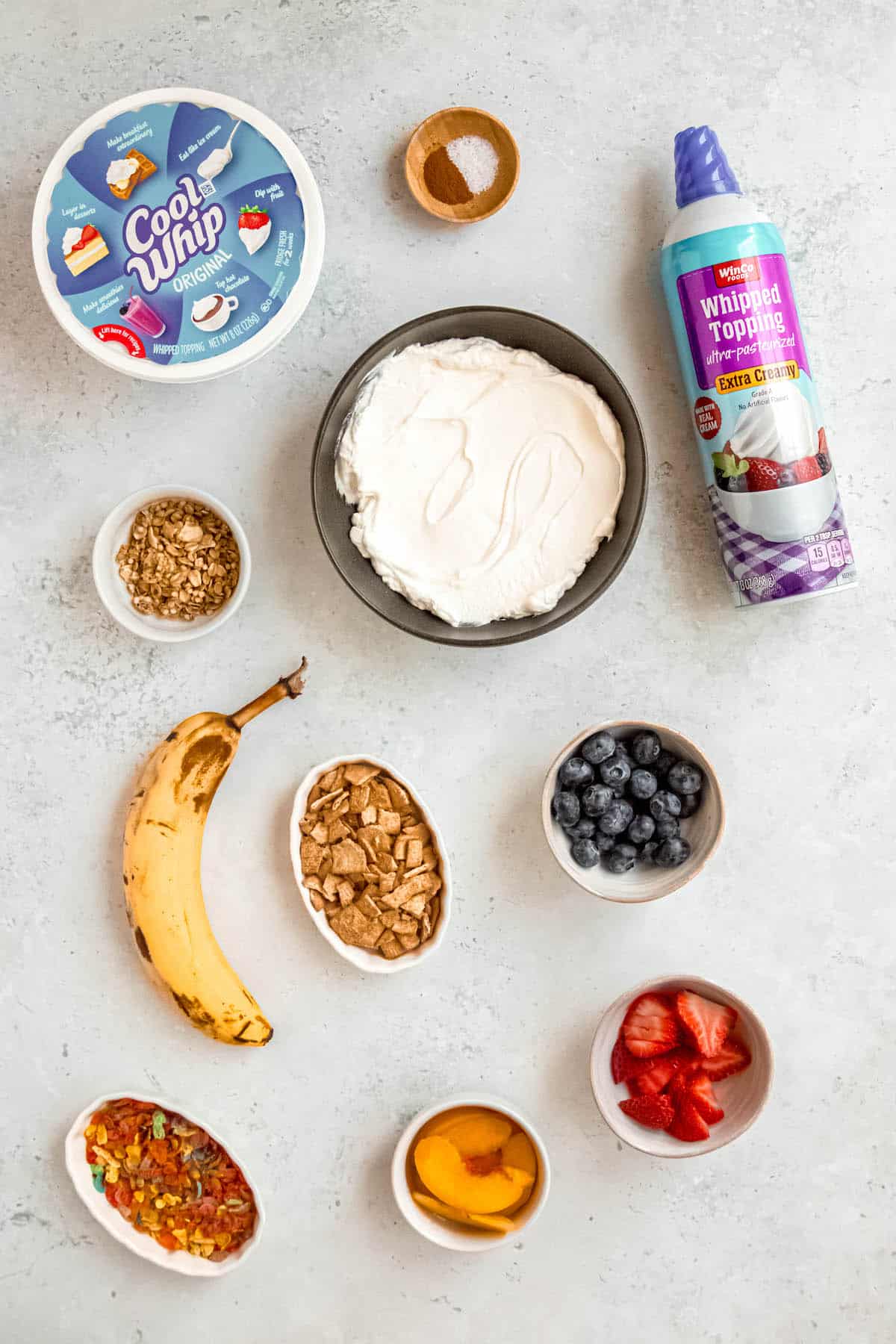 ingredients needed to make breakfast banana split bowls measured out on a white table.