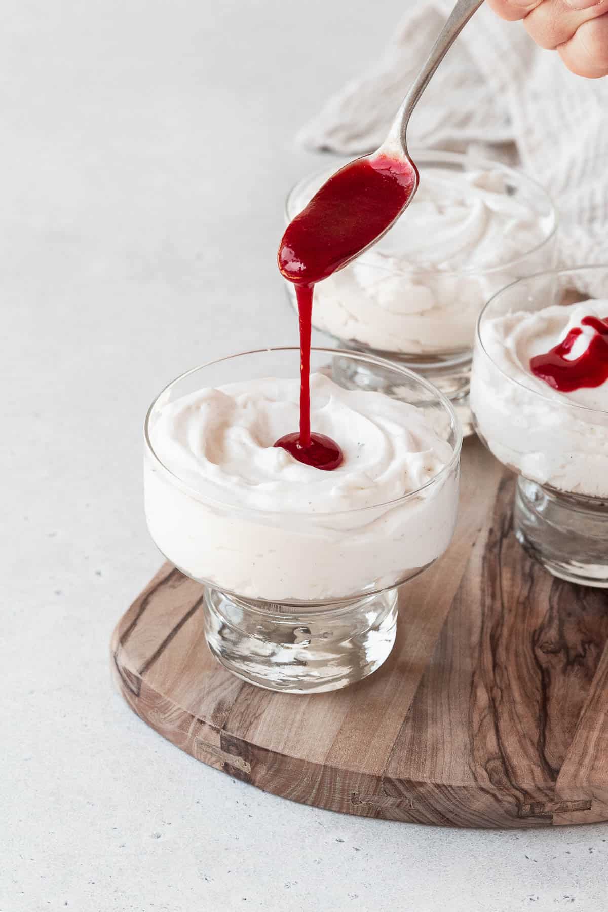 action hero shot of drizzling raspberry coulis onto a serving of French cream cheese mousse.