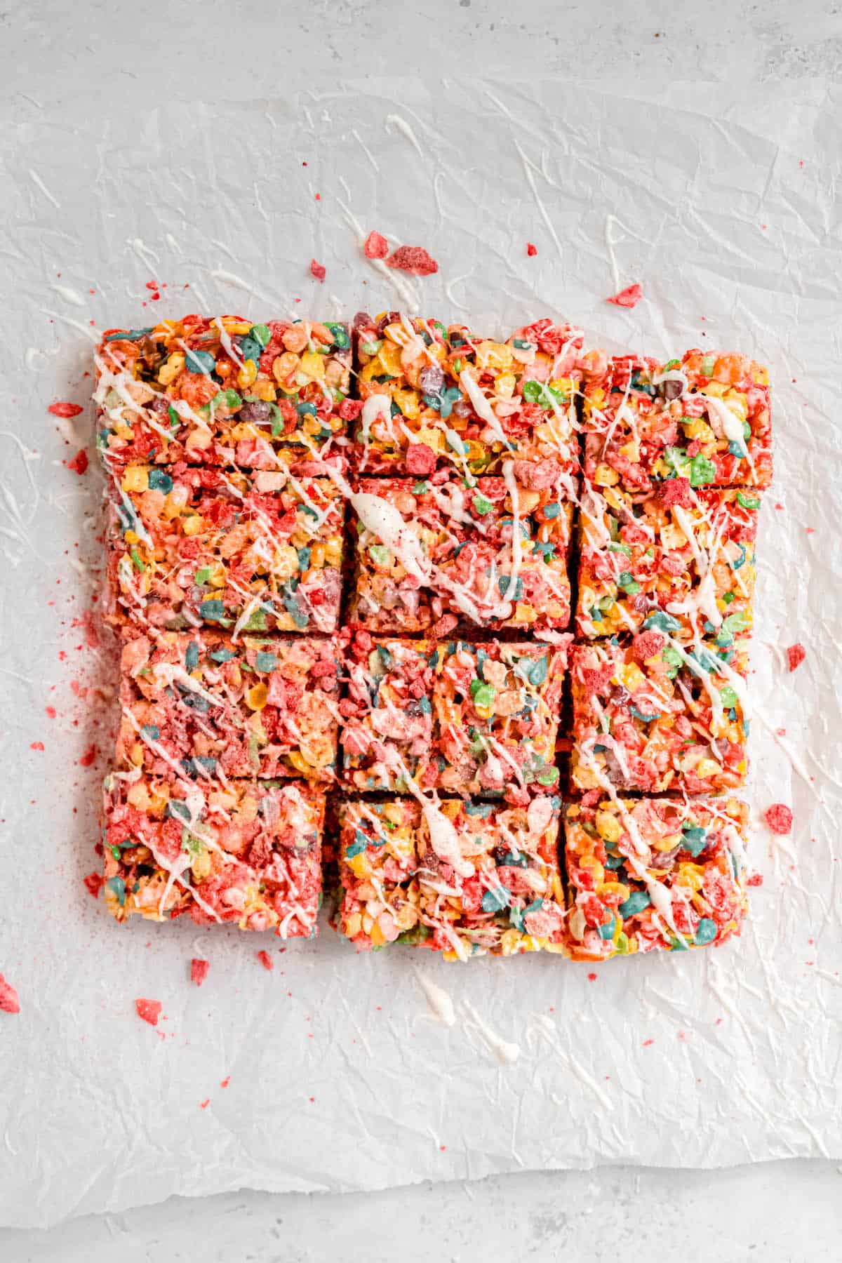 white chocolate drizzled fruity pebbles cereal bars on a crumpled piece of white parchment paper.
