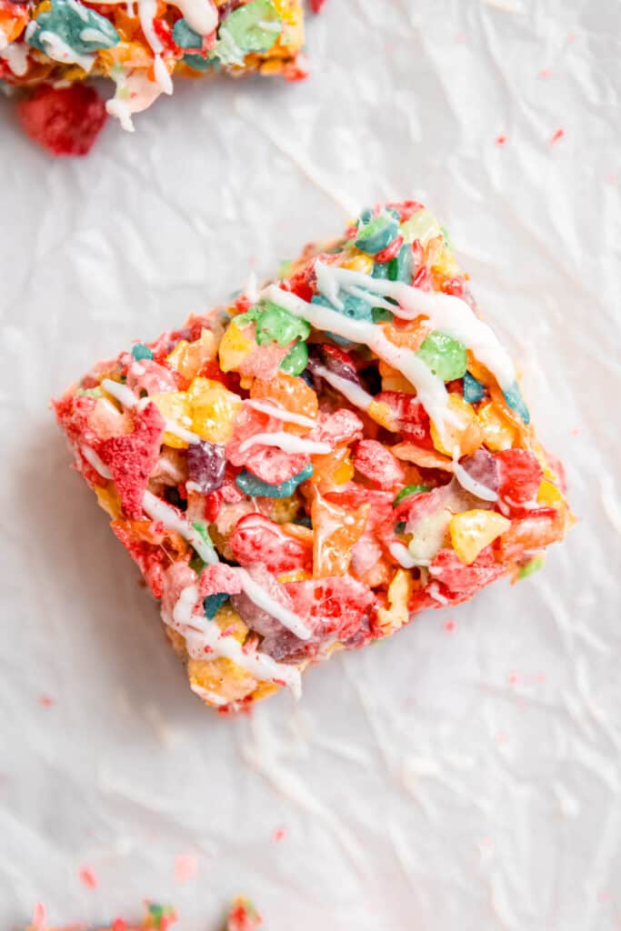 closeup shot of a fruity pebbles cereal bar on a piece of white parchment after being drizzled with strawberry white chocolate decoration.