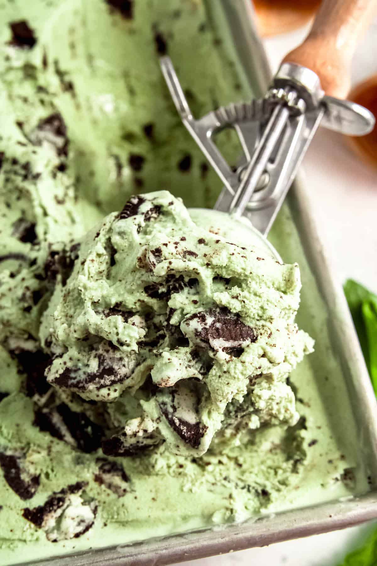overhead closeup shot of a scoop of mint cookies and cream ice cream being scooped from the container after freezing.