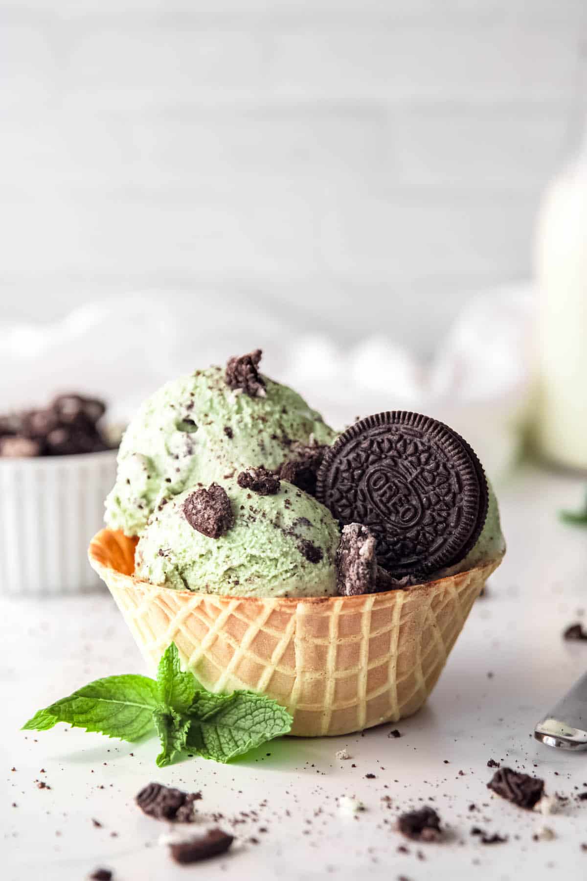 closeup shot of a waffle cone bowl of mint cookies and cream ice cream with an oreo cookie garnish.