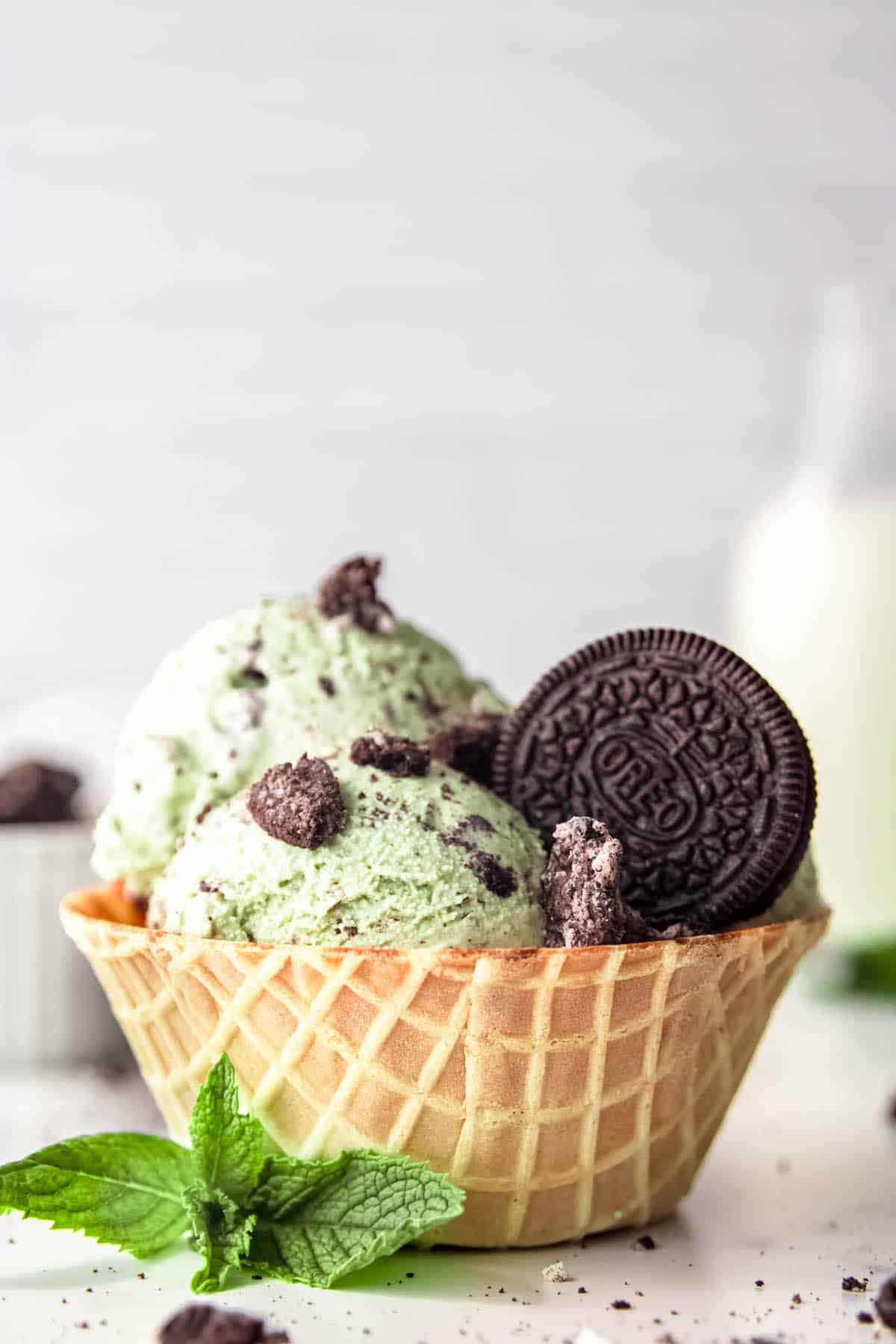 side on shot of a waffle cone bowl filled with 3 scoops of mint cookies and cream ice cream.
