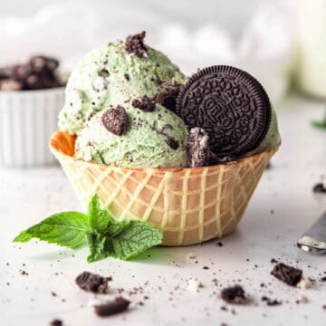 square hero image of 3 scoops of mint cookies and cream ice cream in a waffle cone bowl with a spring of mint and a whole oreo.