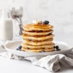 stack of muffin mix pancakes on a white plate with maple syrup being poured on.