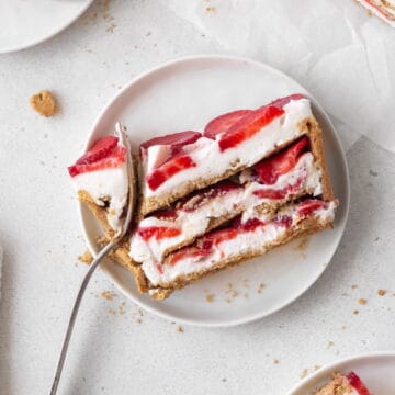 square hero image of a slice of no-bake strawberry cream cheese icebox cake on a white plate with a silver fork taking a bite out.