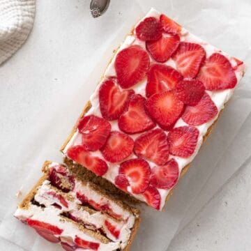 overhead shot of strawberry cream cheese icebox cake on a piece of parchment with one slice tipped over to show the layers of the no-bake strawberry graham cracker dessert.