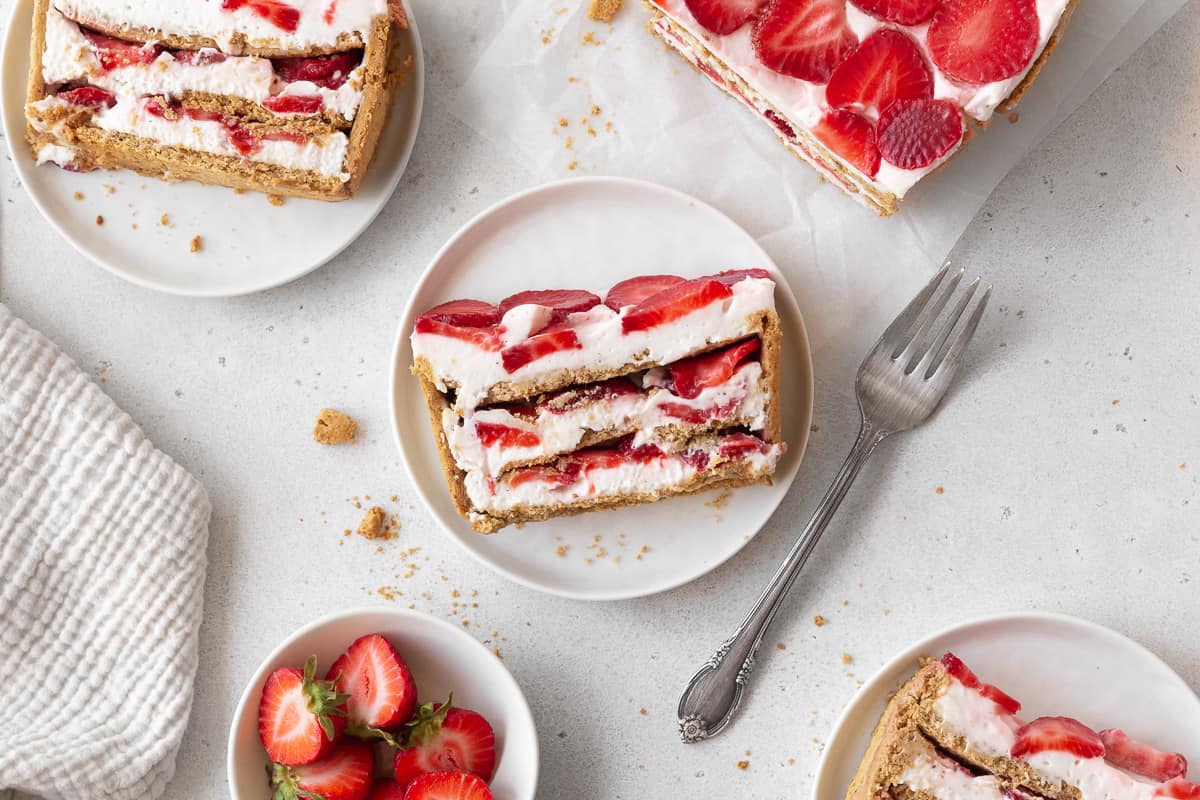 horizontal hero image of a table with 3 dessert plates with slices of strawberry cream cheese icebox cake.