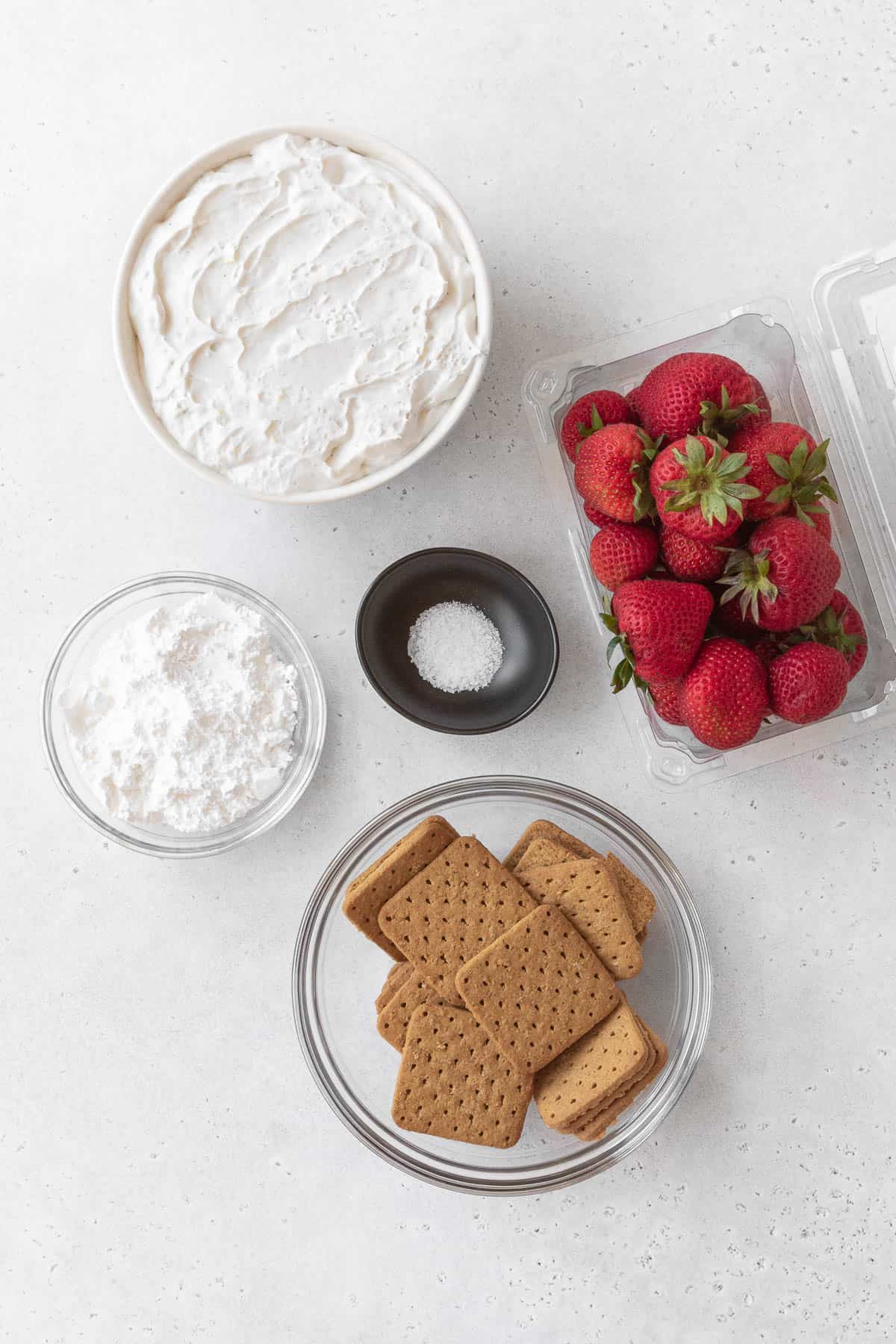 ingredients for strawberry cream cheese icebox cake measured out into bowls on a white table.