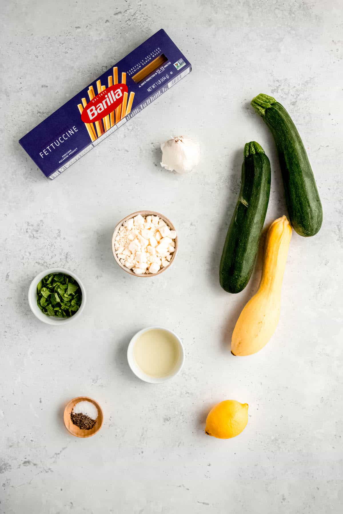 ingredients needed to make zucchini linguine summer pasta laid out ona. white table.