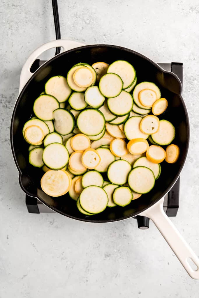 zucchini and summer squash rounds added to a skillet with olive oil and salt.