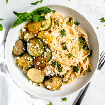 square hero image of a pasta bowl filled with lemony zucchini linguine and garnished with mint and feta.