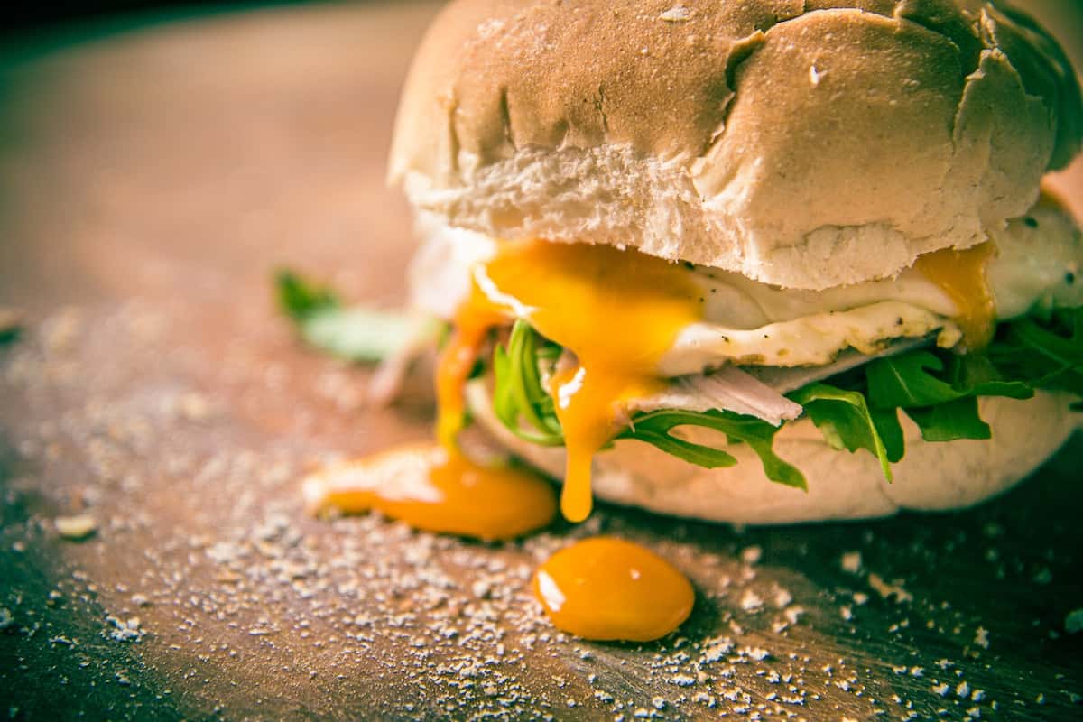 DIY bodega style egg sandwich with egg yolk dripping onto a cutting board.