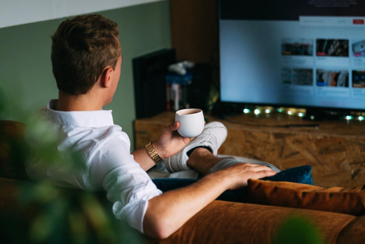 young college student drinking a cup of coffee on the dorm couch.