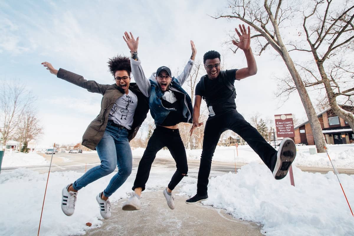 three young adults jumping for glee in the middle of a college campus.