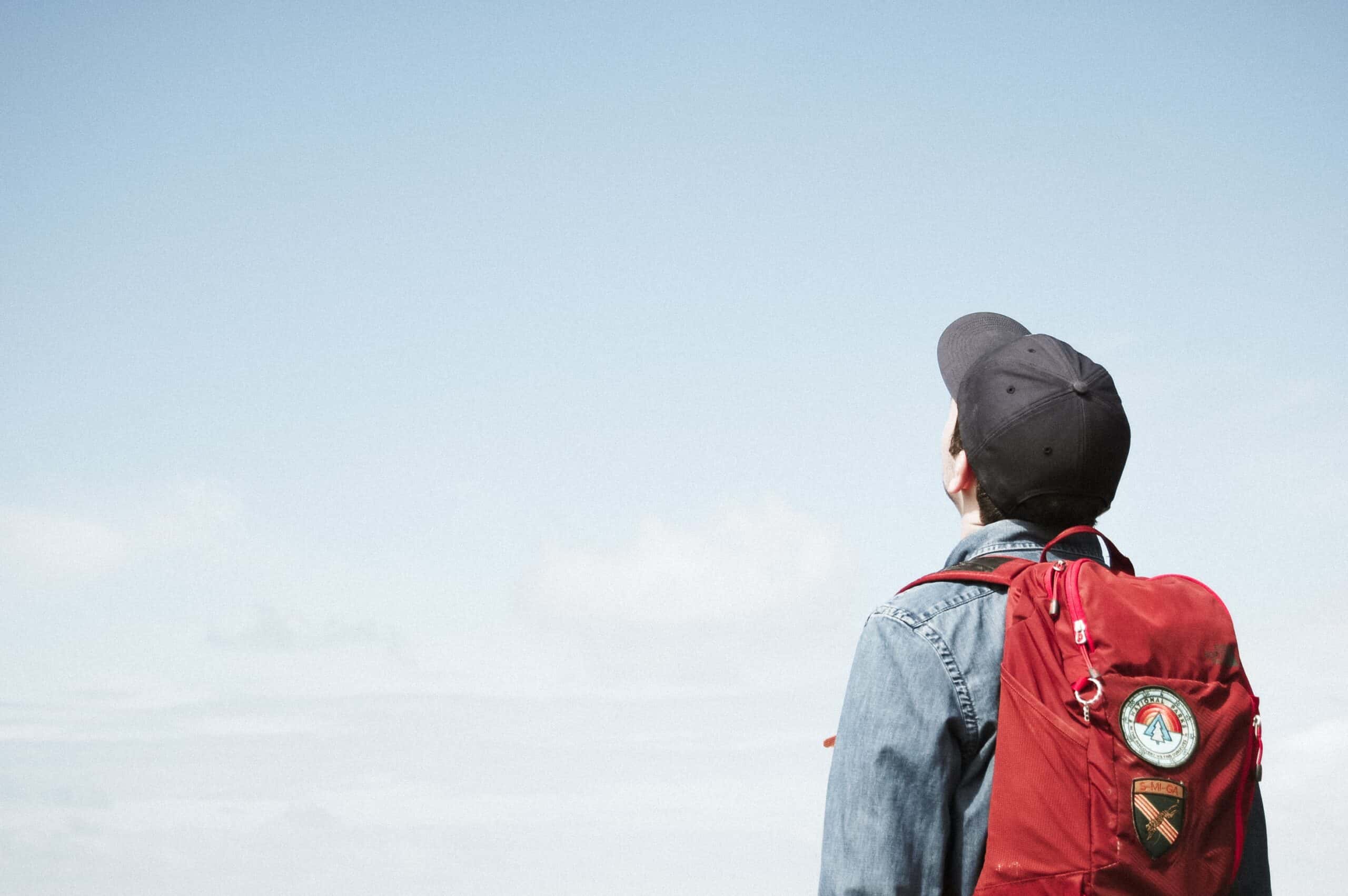 college kid wearing a red backpack while staring up at the sky.