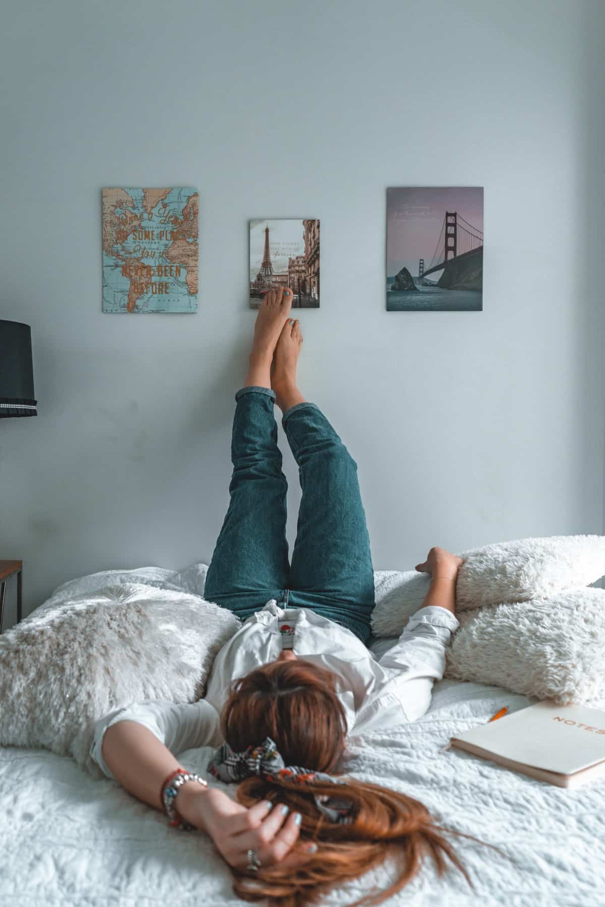 college girl laying on a bed with her feet on the wall with posters above her.