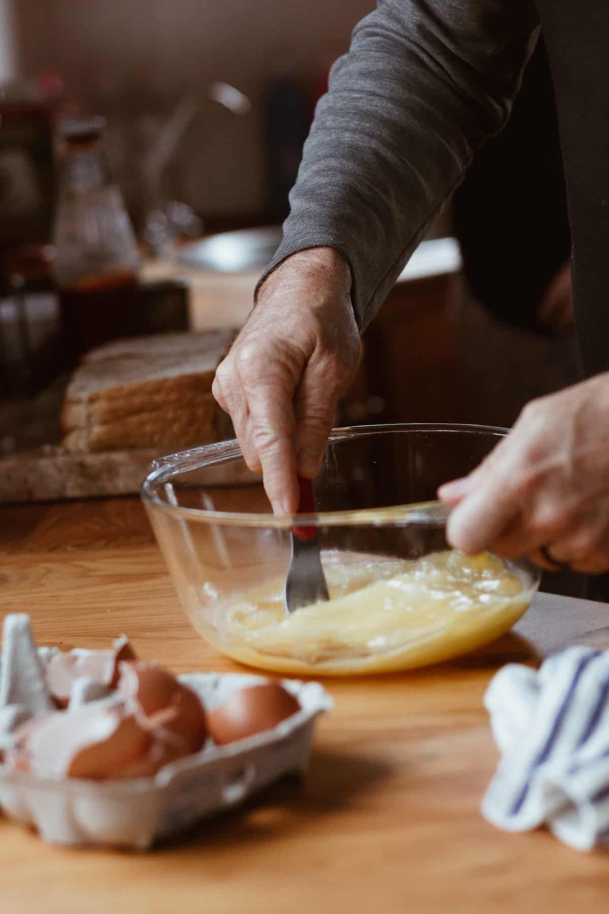 man scrambling eggs in a clear bowl.