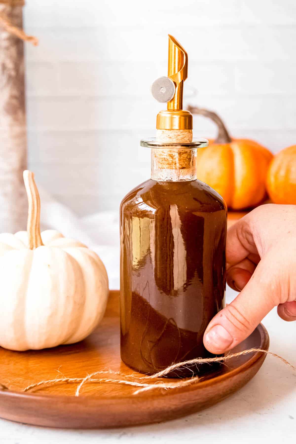 hand grabbing a stoppered bottle of copycat starbucks pumpkin sauce on a wooden tray.