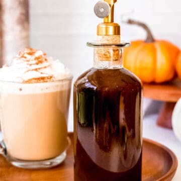 stoppered jar of homemade sugar-free pumpkin sauce on a wooden tray next to a mug of a homemade pumpkin spice latte topped with whipped cream.