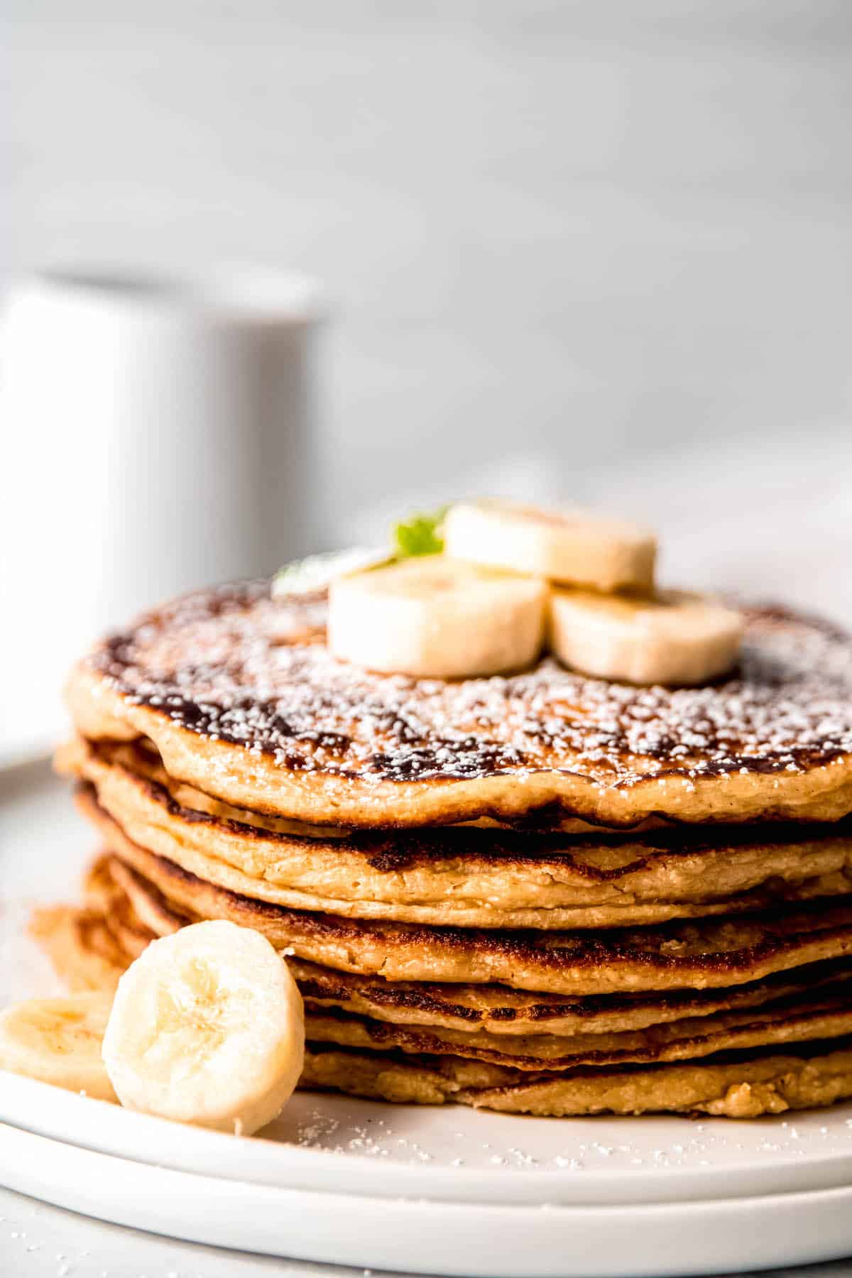 closeup side on shot of a stack of golden brown cottage cheese oatmeal banana protein pancakes topped with powdered sugar and banana slices.